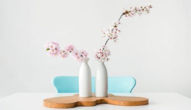 two pink petaled flowers in white vases on brown wooden surface