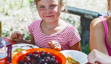 girl in red and white striped shirt holding white ceramic bowl with red and black fruits