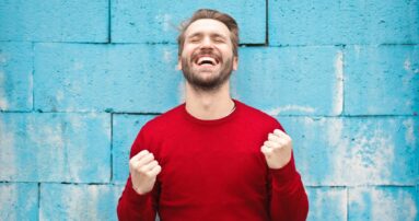 man wearing red long-sleeved shirt standing beside wall
