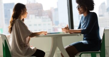 two women sitting beside table and talking