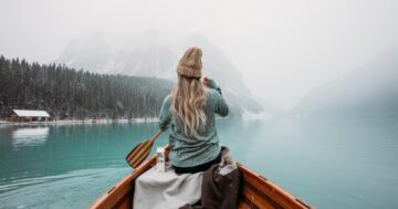 woman in gray hoodie sitting on brown wooden boat on lake during daytime